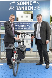 An der Schnellladestationen können auch E-Bikes aufgetankt werden: SPD-Ratsherr Philipp Tacer und MdB Andreas Rimkus haben sich den Tankvorgang für ein E-Bike angeschaut.